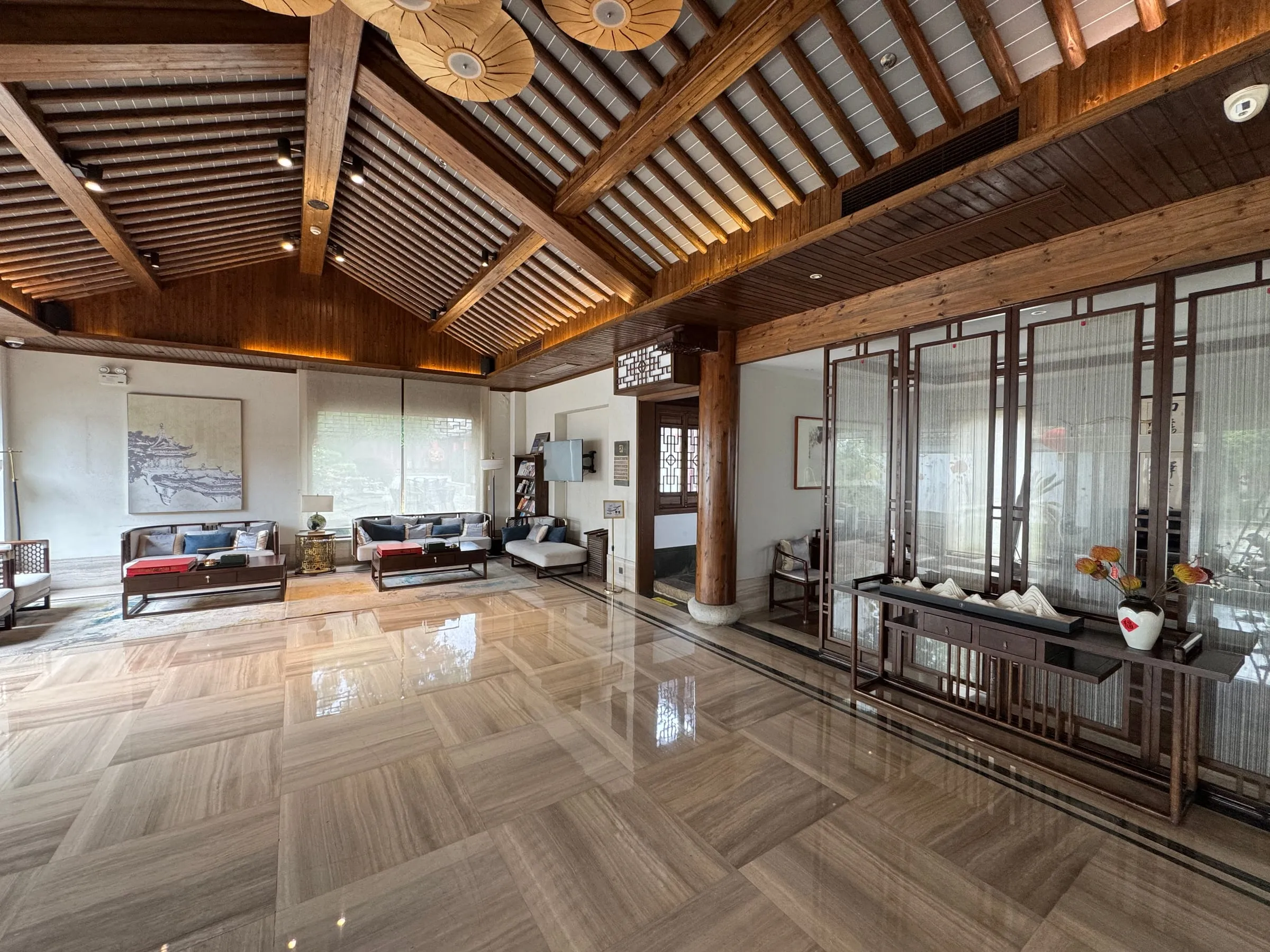 A lobby under exposed timber roof beams, with lattice screens and sofas on a polished stone floor