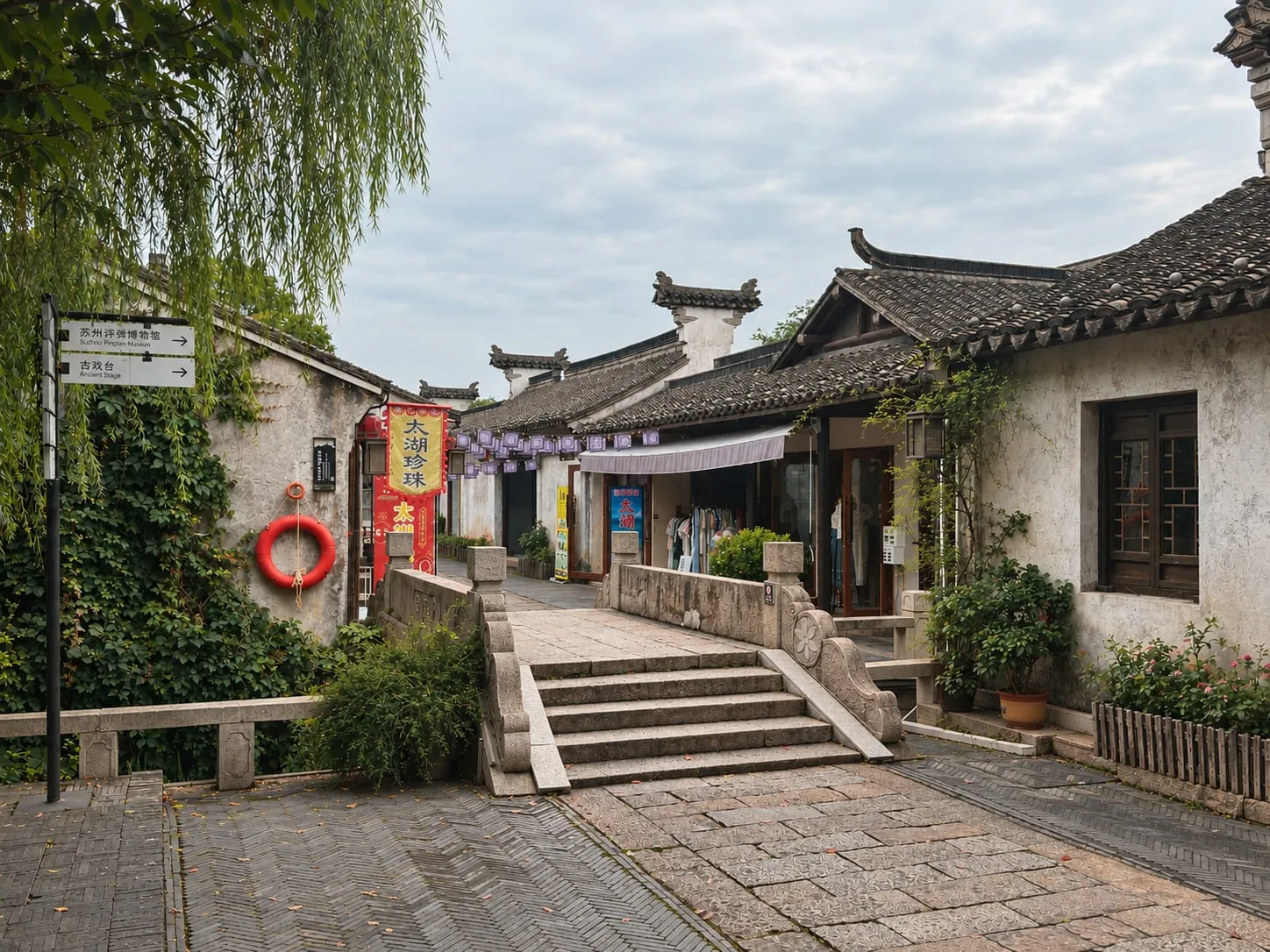 Stone steps over a small bridge into a lane of tiled-roof shops hung with banners